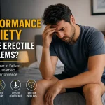 Thoughtful man sitting on the edge of a bed while his partner looks concerned, representing sexual performance anxiety and erection problems